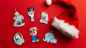 Assorted personalized baby's first Christmas ornaments with Santa hat on red background, featuring diverse characters and holiday themes