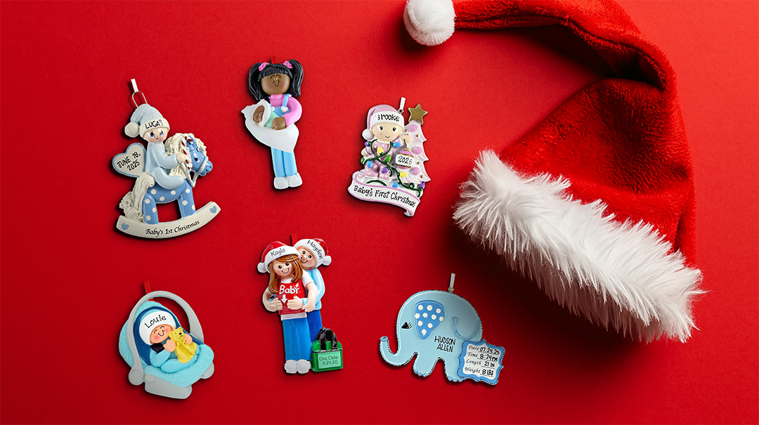 Assorted personalized baby's first Christmas ornaments with Santa hat on red background, featuring diverse characters and holiday themes
