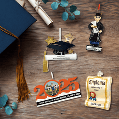 Graduation ornament collection displayed on a wood background with caps, tassels, and diplomas. Includes personalized cap-and-diploma ornaments, a scroll diploma ornament, a 2025 photo ornament, and a graduate figurine.