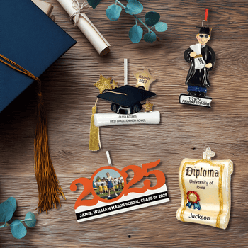Graduation ornament collection displayed on a wood background with caps, tassels, and diplomas. Includes personalized cap-and-diploma ornaments, a scroll diploma ornament, a 2025 photo ornament, and a graduate figurine.