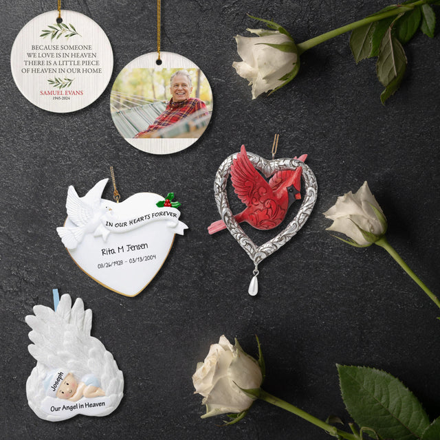 Memorial Christmas ornament collection displayed with white roses. Includes a memorial quote ornament, photo ornament, heart ornament with dove, silver heart with red cardinal, and angel wings ornament.