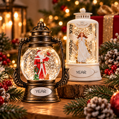 Christmas snow globes featuring a Santa lantern snow globe and an angel snow globe, displayed with festive greenery, pinecones, and warm holiday lights.