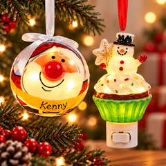 Personalized light-up Christmas ornaments featuring a glowing Santa ornament with the name Kenny and a festive snowman cupcake night light, displayed with Christmas greenery and warm holiday lights.