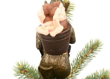 Krampus Christmas tree topper featuring a horned folklore figure with a long red tongue, black chain, branches, and child on his back.
