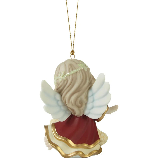 Precious Moments Christmas ornament featuring an angel with white wings watching over a sleeping baby in a manger-style bed.