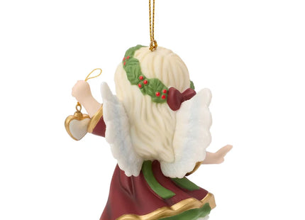 Precious Moments Christmas angel ornament featuring a blonde angel in burgundy and green holding a small heart ornament decorated with holly.