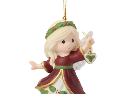 Precious Moments Christmas angel ornament featuring a blonde angel in burgundy and green holding a small heart ornament decorated with holly.