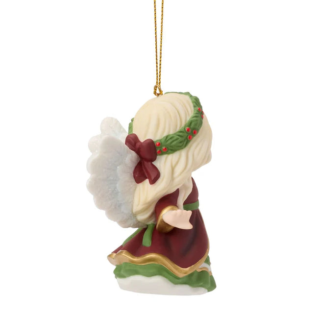 Precious Moments Christmas angel ornament featuring a blonde angel in burgundy and green holding a small heart ornament decorated with holly.