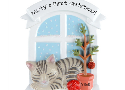 Personalized gray tabby cat first Christmas ornament by a snowy window with custom name and year.
