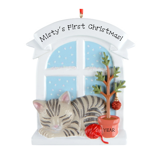 Personalized gray tabby cat first Christmas ornament by a snowy window with custom name and year.