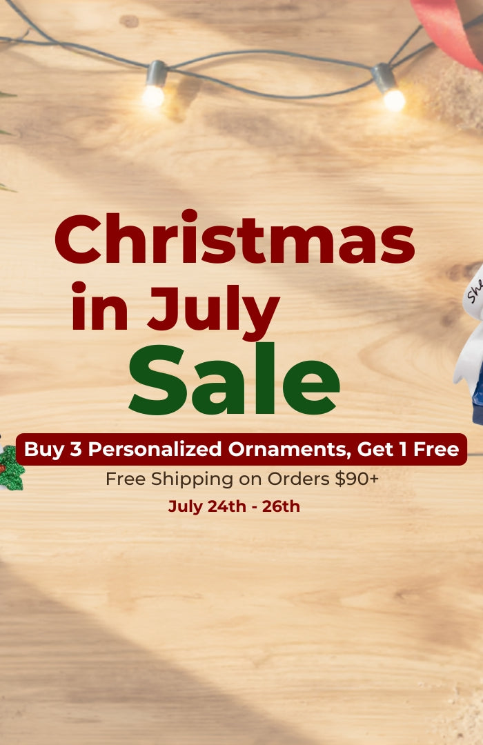 Promotional sale graphic for Christmas personalized ornaments, featuring several festive ornament designs on a wood-textured background with palm leaves, string lights, ribbons, and sale text reading 'Christmas in July Sale' and 'Buy 3 Personalized Ornaments, Get 1 Free'.